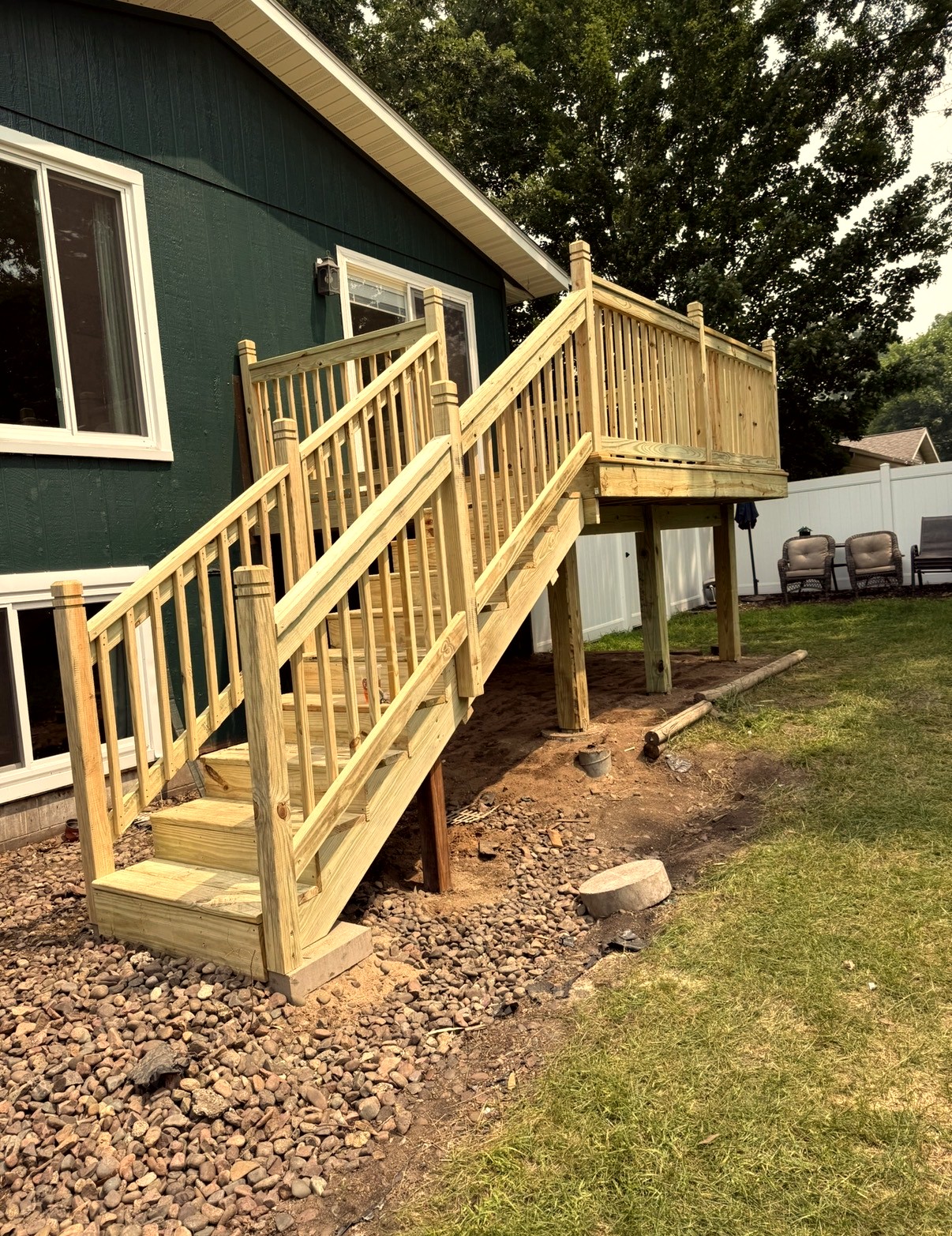 Newly built wooden deck with stairs and railings beside a dark green house